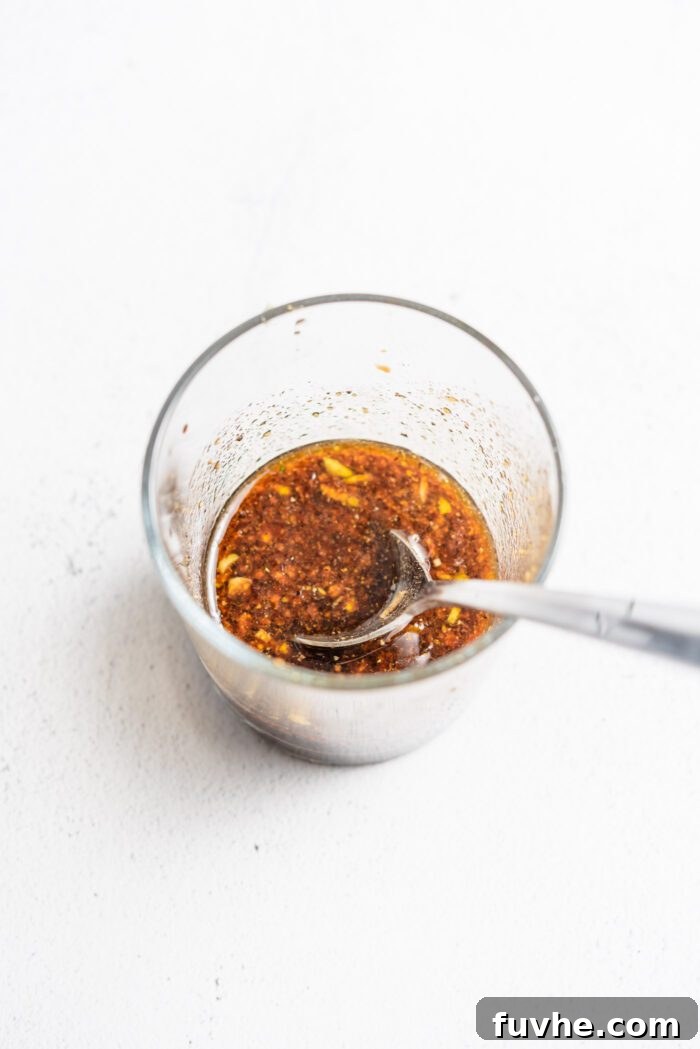 Homemade balsamic dressing in a small glass cup with a spoon resting in it, ready to be poured.