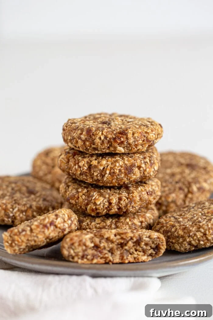 Tahini Date Gems 6 4 oat date cookies stacked on a plate. More cookies sit around the stack.
