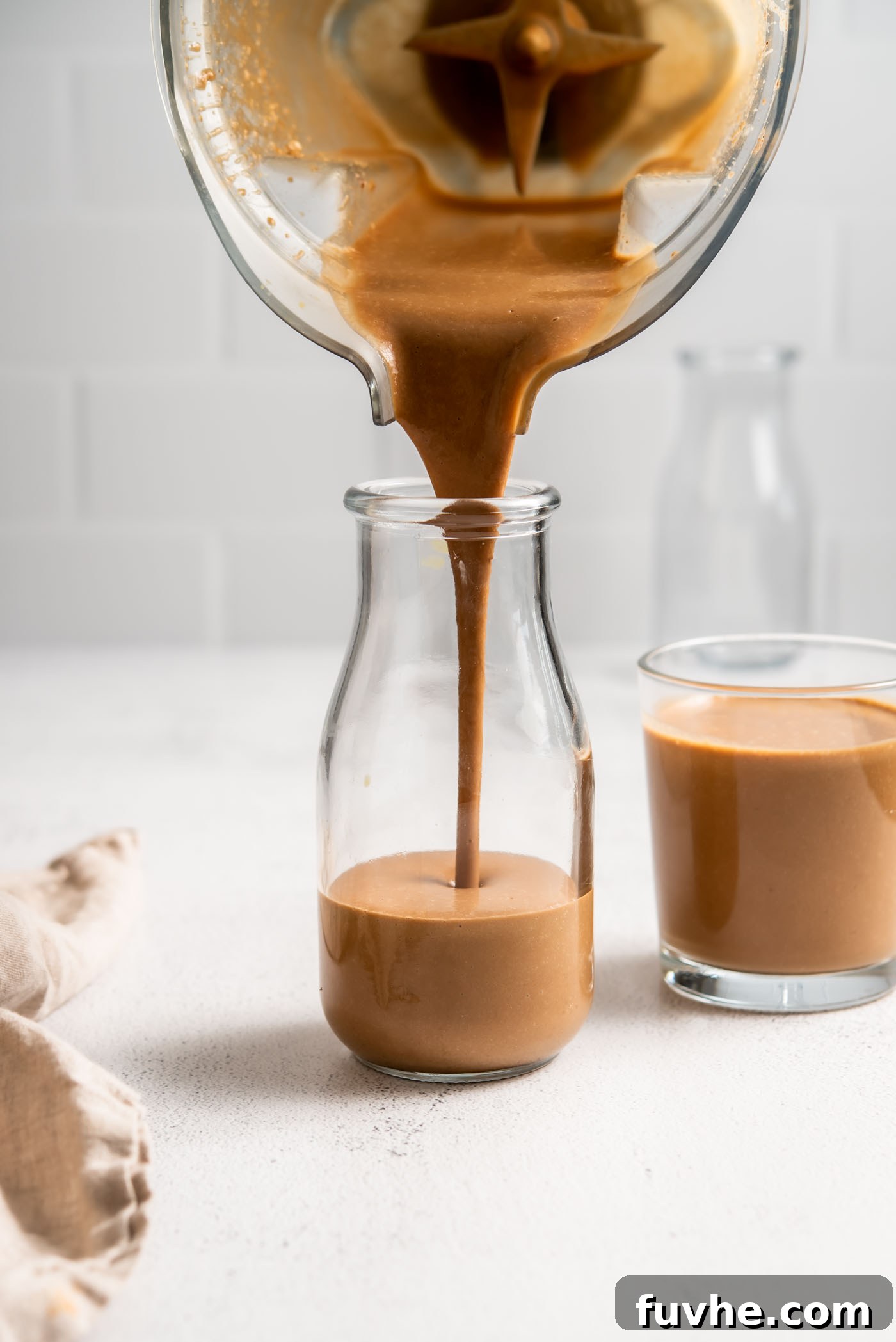 Decadent Tiramisu Smoothie 2 A refreshing Tiramisu Protein Smoothie being poured into an elegant glass jar, showcasing its rich, creamy texture and dark chocolate color.