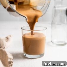 A high-speed blender pouring a creamy chocolate Tiramisu Protein Smoothie into a glass.