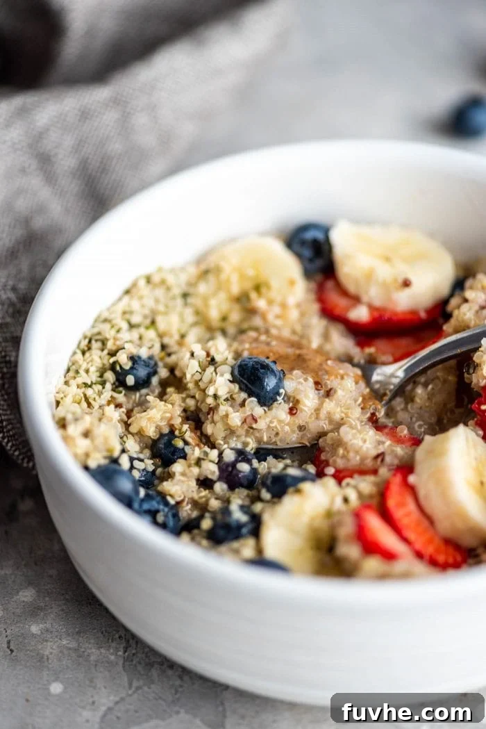 Easy breakfast quinoa in a white bowl with hemp seeds, almond butter, berries and banana. A vibrant bowl of breakfast quinoa, garnished with fresh berries, sliced banana, crunchy hemp seeds, and a drizzle of almond butter, showcasing a quick and healthy meal.