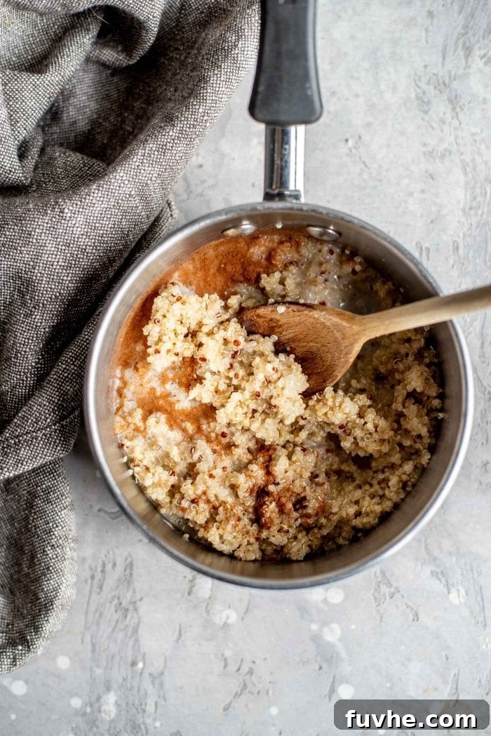 Cooked quinoa with cinnamon and almond milk in a small saucepan with a wooden spoon. A small saucepan filled with cooked quinoa, infused with cinnamon and almond milk, ready to be simmered into a delightful breakfast porridge.