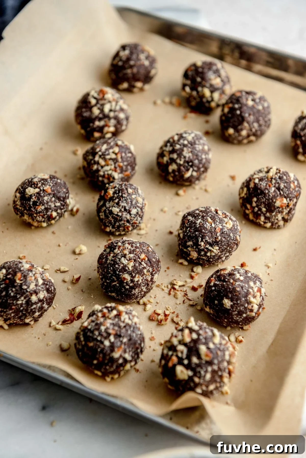 Chocolate Date Truffles 5 A baking tray filled with perfectly formed chocolate date balls, each evenly coated in finely crushed pecans, showcasing their appealing texture and ready for chilling.