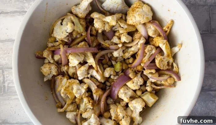 Spiced Cauliflower Power Bowl 4 Chopped cauliflower, red onion and chickpeas mixed with curry powder and other spices in a bowl. Ready for roasting to achieve perfect caramelization.