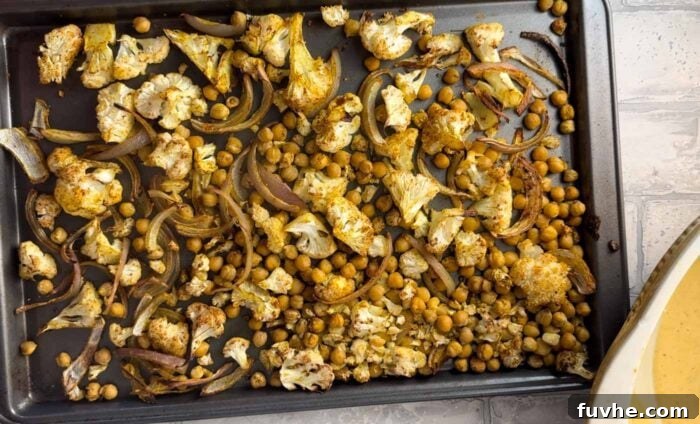 Spiced Cauliflower Power Bowl 5 Roasted cauliflower, chickpeas and red onion coated in curry powder and other spices on a baking sheet. Crispy and golden brown, ready to be incorporated into the salad.