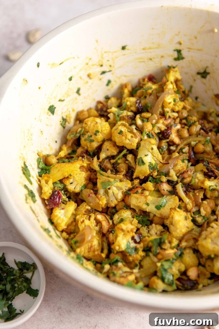 Spiced Cauliflower Power Bowl 7 A curry roasted cauliflower salad with chickpeas, red onion, cilantro, cashews and cranberries in a large bowl. A complete and vibrant salad, ready to be served.