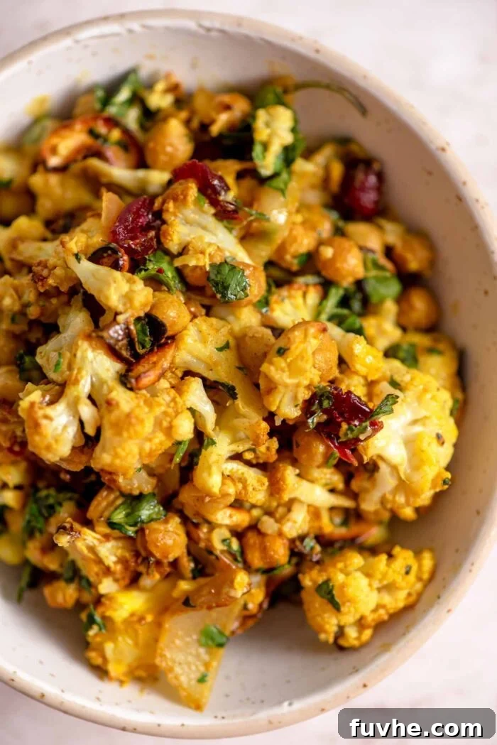 Spiced Cauliflower Power Bowl 8 Close up overhead view of a small bowl of curried roasted cauliflower salad with onion slices, chickpeas and cranberries in a creamy curry dressing. A tempting, detailed shot highlighting the textures and vibrant colors.