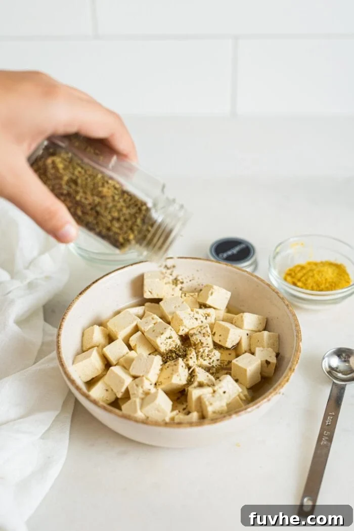 Vibrant Mediterranean Quinoa Bowls 4 Cubed tofu feta being seasoned with dried oregano, next to a spoon and a dish of nutritional yeast.