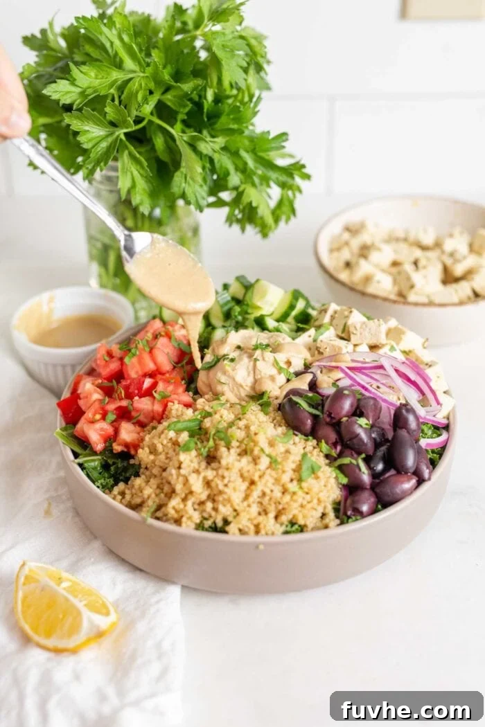 Vibrant Mediterranean Quinoa Bowls 7 A spoonful of tahini being drizzled over a vibrant Mediterranean quinoa bowl filled with quinoa, chopped vegetables, red onion, olives, and tofu feta.