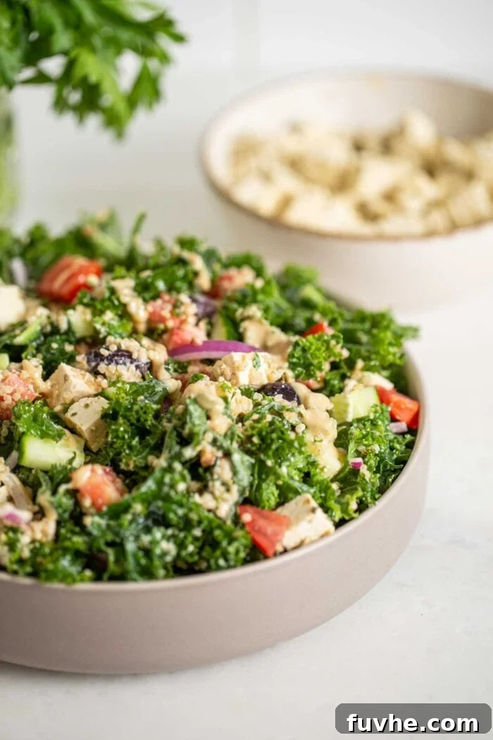 Vibrant Mediterranean Quinoa Bowls 8 A close-up of a beautifully composed kale salad bowl featuring quinoa, tofu feta, fresh tomatoes, cucumber, and pickled red onion, with more tofu in the background.