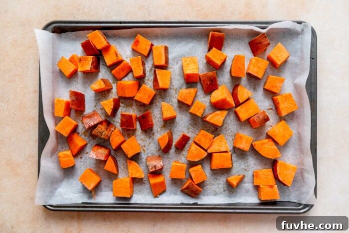 Cubed sweet potatoes seasoned with spices and olive oil, spread out on a baking sheet lined with parchment paper, ready for roasting.