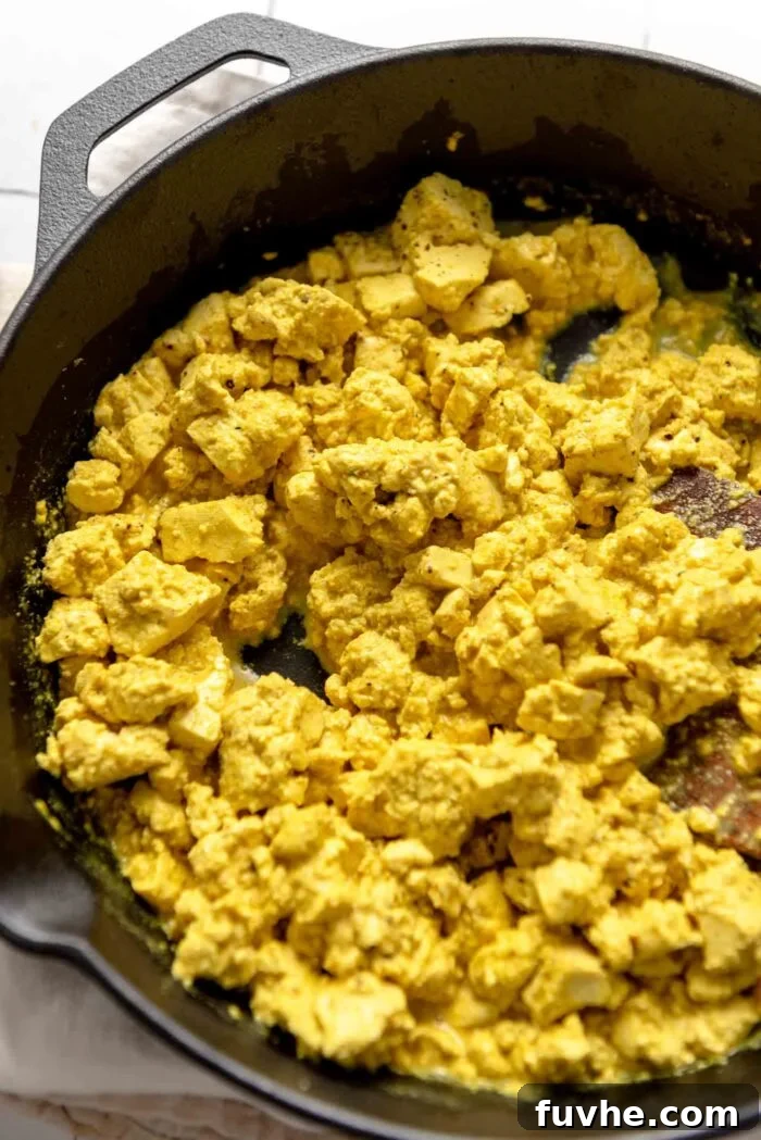 A close-up shot of crumbled tofu cooking in a skillet, turning golden brown before the sauce is added.