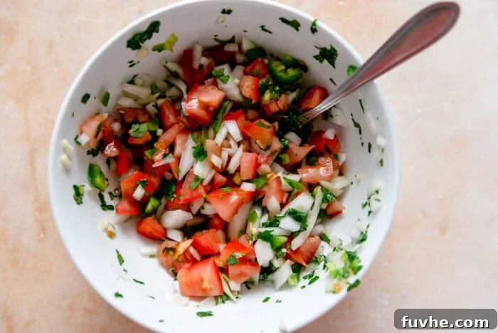 A colorful mixing bowl filled with freshly prepared salsa, featuring diced tomatoes, finely chopped red onion, and sliced green jalapeños, ready to be mixed.