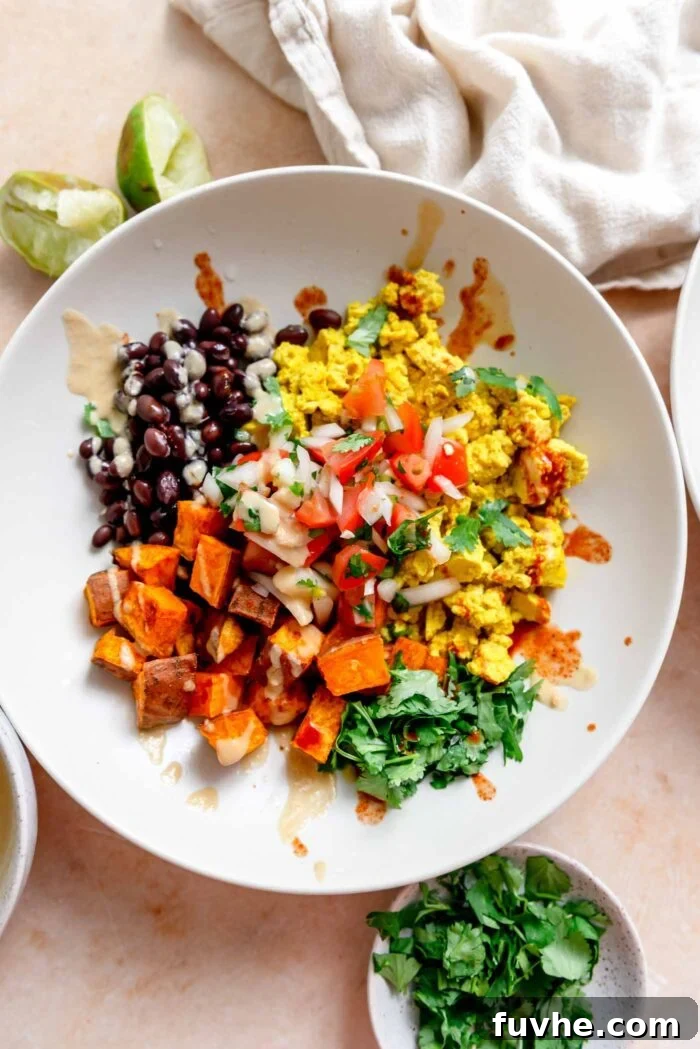 A vibrant breakfast burrito bowl, topped with fresh cilantro, a golden tofu scramble, black beans, roasted sweet potato, creamy chipotle sauce, and a fiery drizzle of hot sauce.