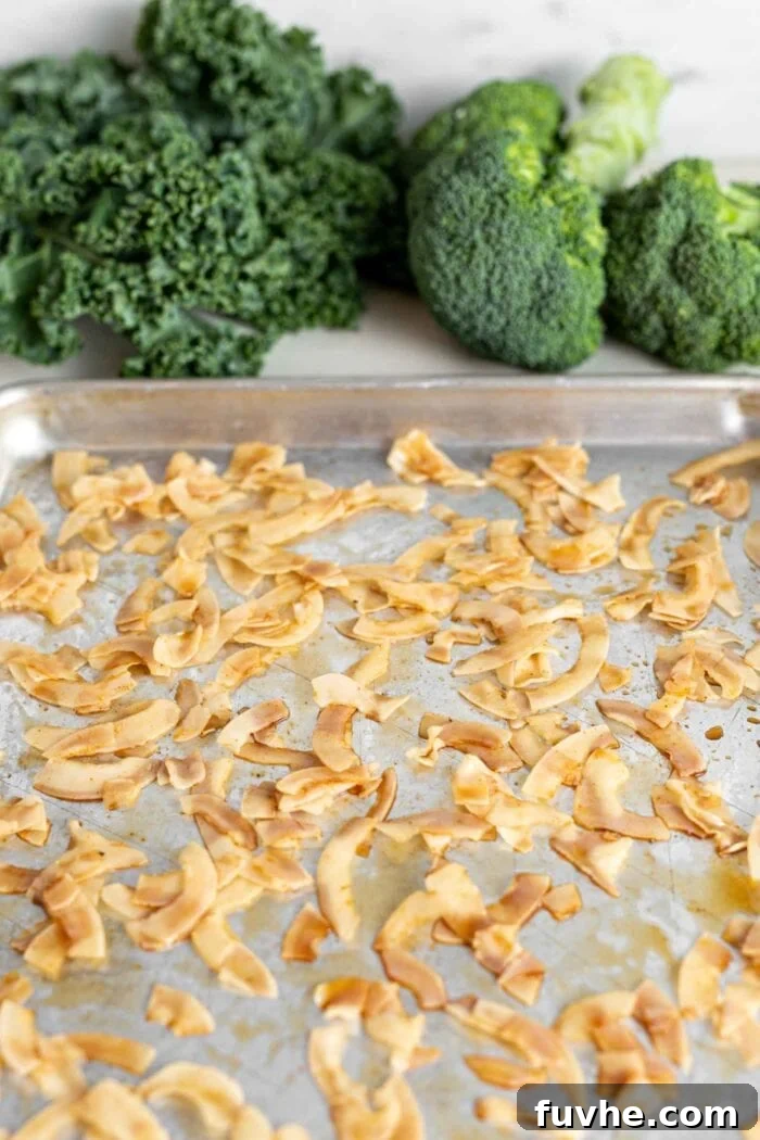 Green Harvest Bowl 5 Unsweetened large coconut flakes spread evenly on a parchment-lined baking tray before baking.