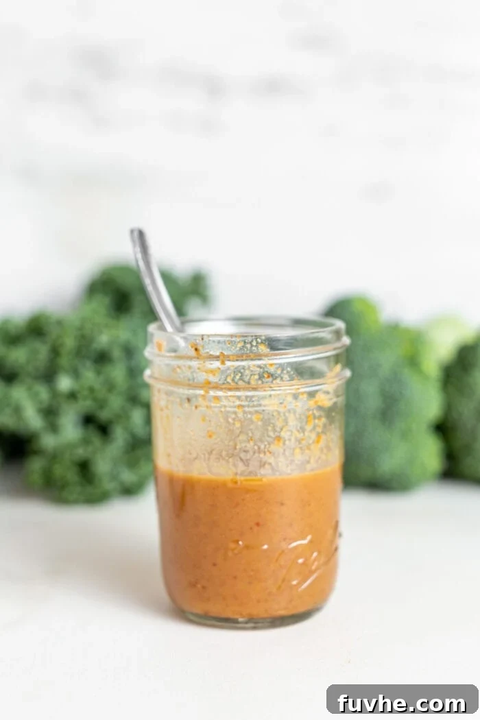 Green Harvest Bowl 7 A smooth, creamy almond butter sauce in a glass jar with a spoon, ready to be drizzled.