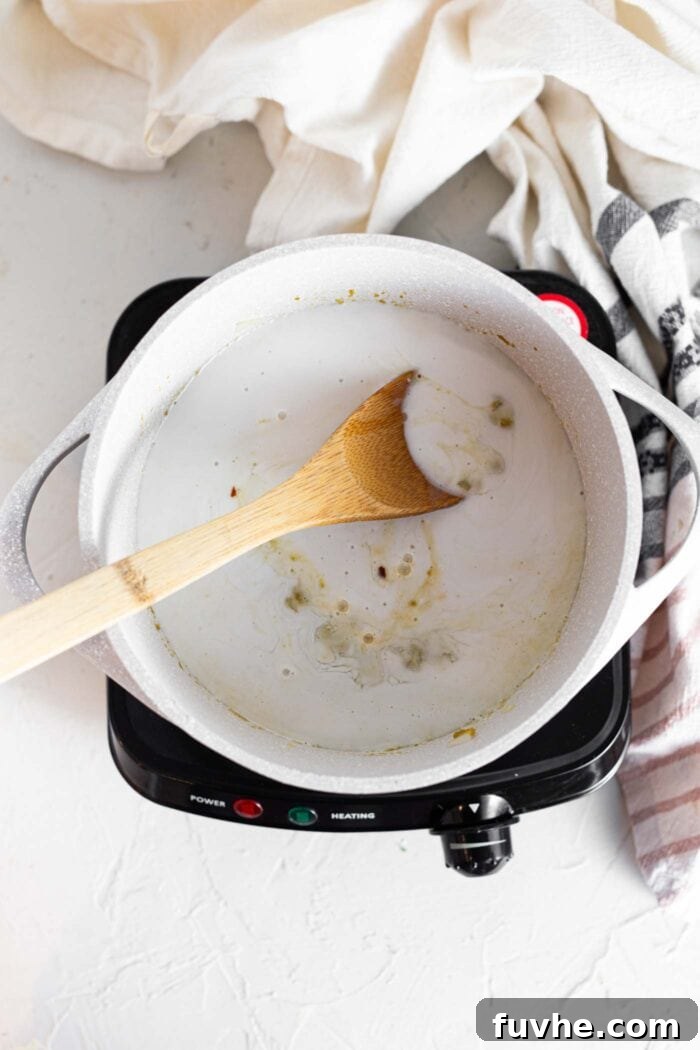 Fragrant Vegan Thai Green Curry 6 A wooden spoon stirring rich coconut milk into a large soup pot filled with vegetables, beginning the simmering process.