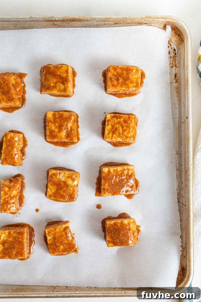 Cubes of tempeh in a peanut butter sauce on a baking pan.