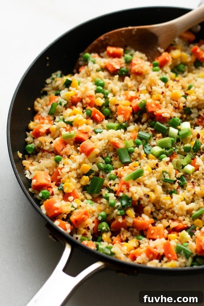 Whipping Up Perfect Cauliflower Rice 7 Cauliflower rice with carrots, peas and corn in a skillet with a wooden spoon.