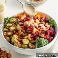 Drizzling a spoon of sauce over a salad with roasted vegetables and kale.