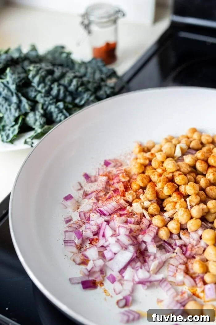 Vibrant Chickpea Kale Stir Fry 5 Close-up of chopped red onion and chickpeas sizzling in a skillet on the stovetop, starting to brown.