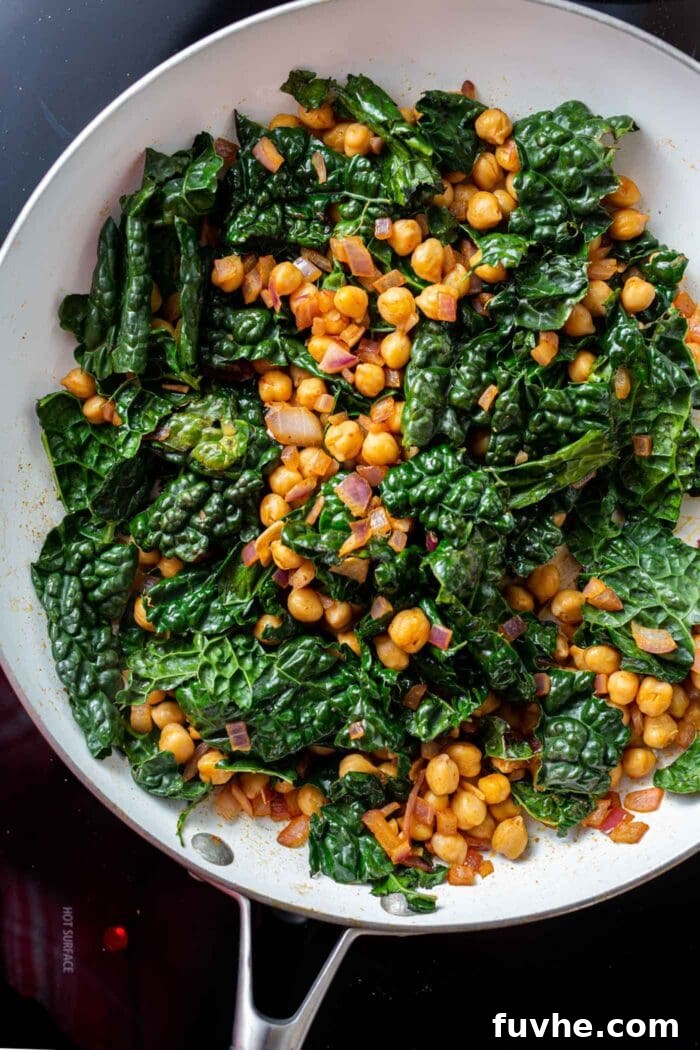 Vibrant Chickpea Kale Stir Fry 6 A colorful kale chickpea stir fry, with wilted kale, in a skillet on the stovetop, glistening with oil and spices.