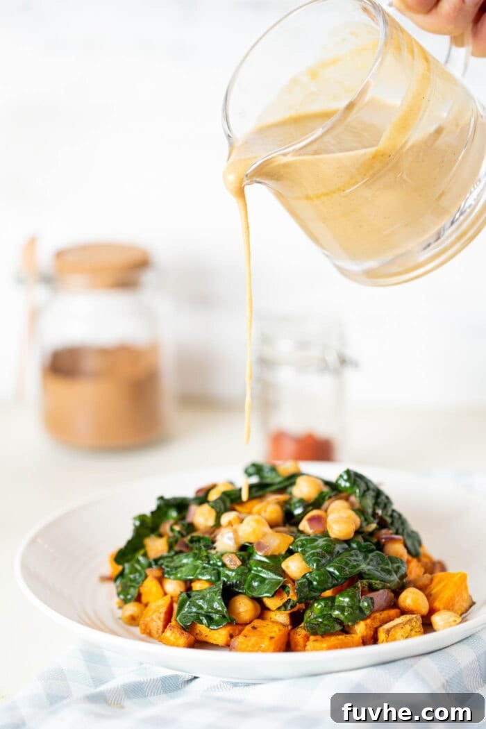 Vibrant Chickpea Kale Stir Fry 7 Miso peanut sauce being poured from a small pitcher over a serving of kale and chickpea stir fry in a white bowl, steam gently rising.