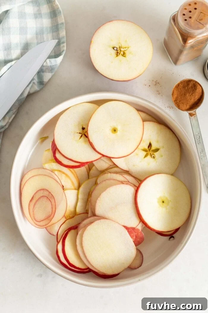 An overhead shot showcasing a beautiful display of perfectly thinly sliced apples in a large bowl, ready for seasoning. The slices are uniform and appear slightly translucent at the edges, indicating ideal preparation.