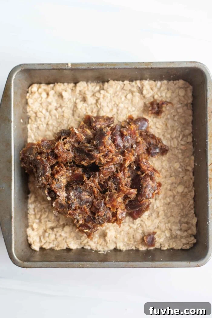 Date paste being carefully spread over a golden oat crust in a baking pan.