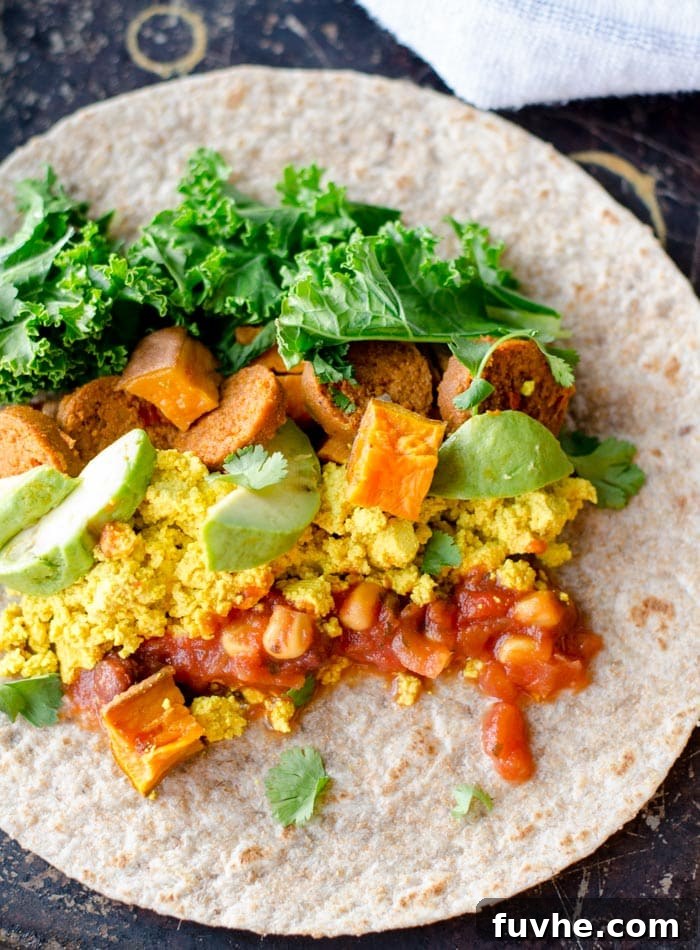Golden Sweet Potato Burritos 4 A close-up of a partially assembled vegan sweet potato breakfast burrito, showcasing the colorful layers of roasted sweet potato, dark green kale, and light tofu scramble nestled inside a tortilla.