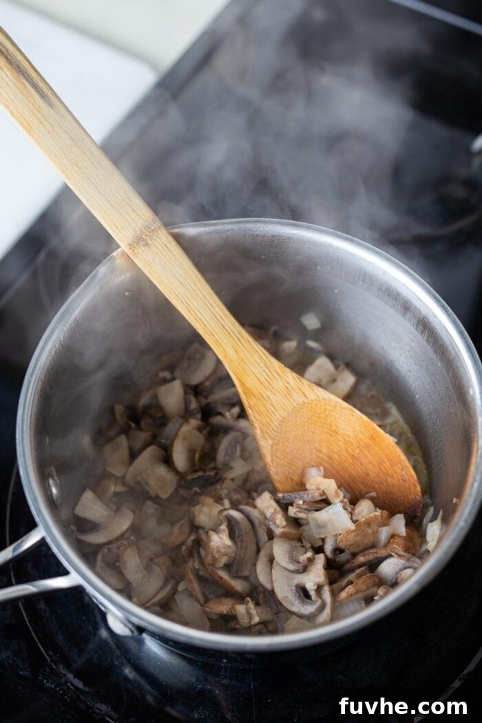 Velvety Vegan Mushroom Gravy 3 Sliced mushrooms and onions gently cooking in a small saucepan on the stovetop, releasing their savory aromas.