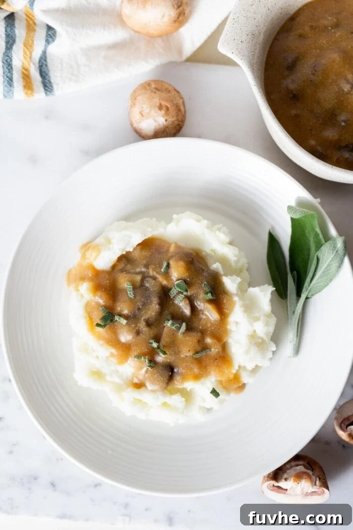 Velvety Vegan Mushroom Gravy 4 A beautifully presented plate of fluffy mashed potatoes, generously draped with rich vegan mushroom gravy, ready to be enjoyed.