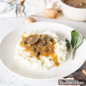 Mushroom gravy over mashed potatoes on a plate with some fresh sage on it.