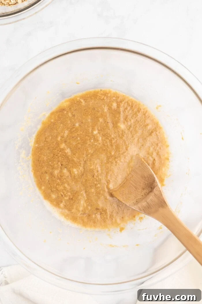 Irresistible Vegan Peanut Butter Oatmeal Cookies 6 A smooth, creamy mixture of mashed banana, peanut butter, almond milk, and maple syrup in a glass mixing bowl, ready for dry ingredients.