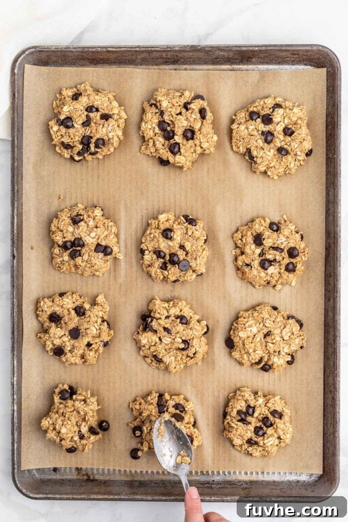 Irresistible Vegan Peanut Butter Oatmeal Cookies 8 Twelve perfectly formed raw vegan peanut butter oatmeal chocolate chip cookies neatly arranged on a parchment paper-lined baking tray, ready for the oven.