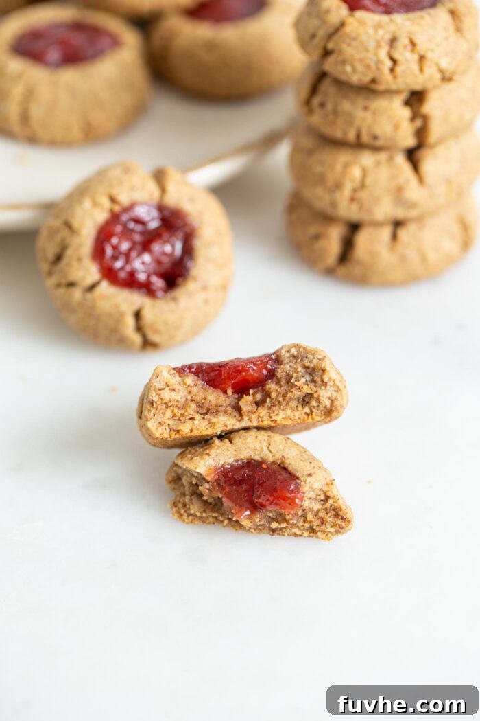 A close-up shot of a broken thumbprint cookie reveals its tender, moist interior texture and the soft jam filling.