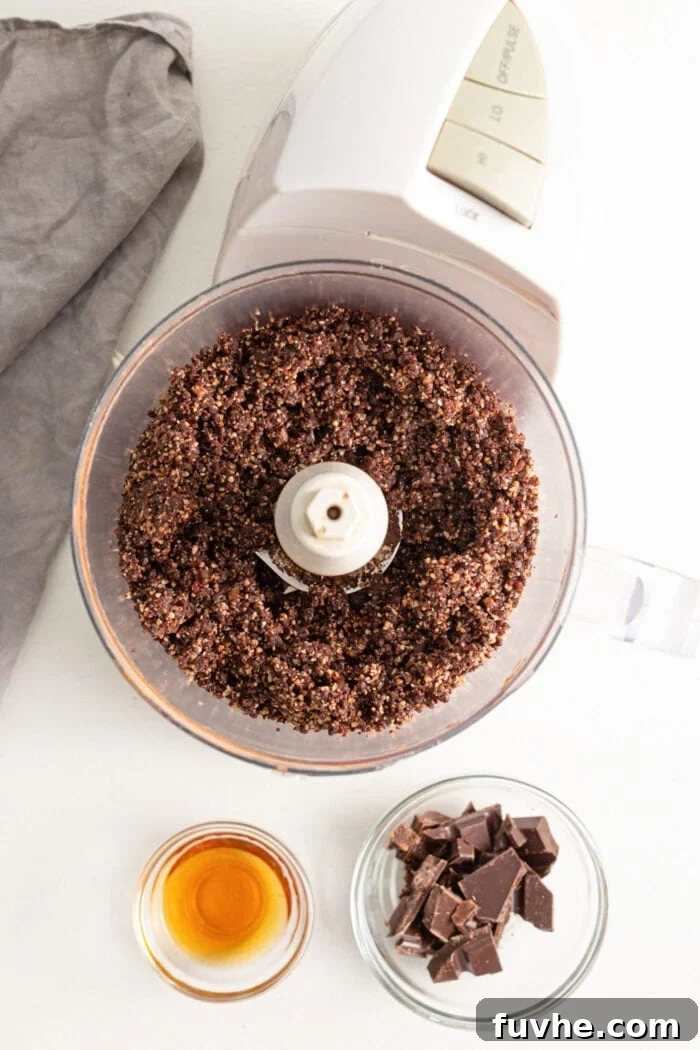 Tipsy Vegan Truffles 5 Dates blended with cocoa powder and pecans in a food processor. Small dish of chocolate beside food processor.