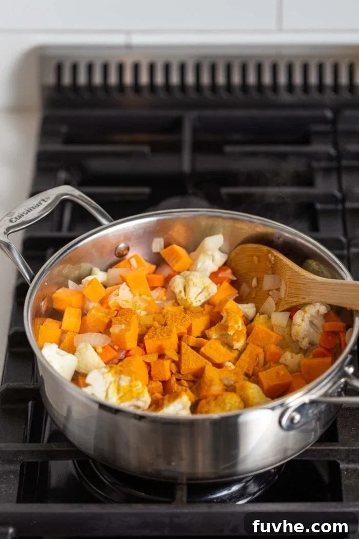 Sweet potato, cauliflower, carrot, onion, garlic, ginger, and turmeric cooking together in a stock pot, infusing the vegetables with vibrant color and flavor.