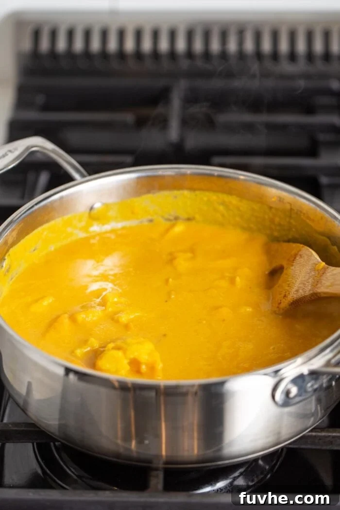 Large pot of creamy sweet potato soup cooking on a gas range stove, with a wooden spoon resting inside, ready to be served.