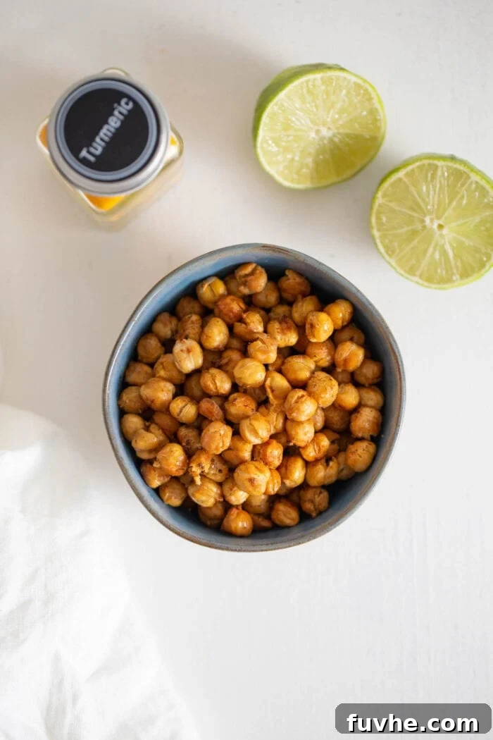 Overhead view of a bowl of perfectly roasted, golden-brown chickpeas, with a freshly cut lime beside it, ready for garnish.