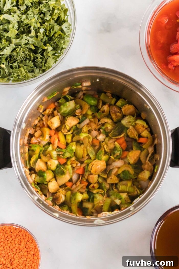 A close-up shot of chopped onion, Brussels sprouts, carrot, and potato cooking gently in a soup pot, releasing their aromas.
