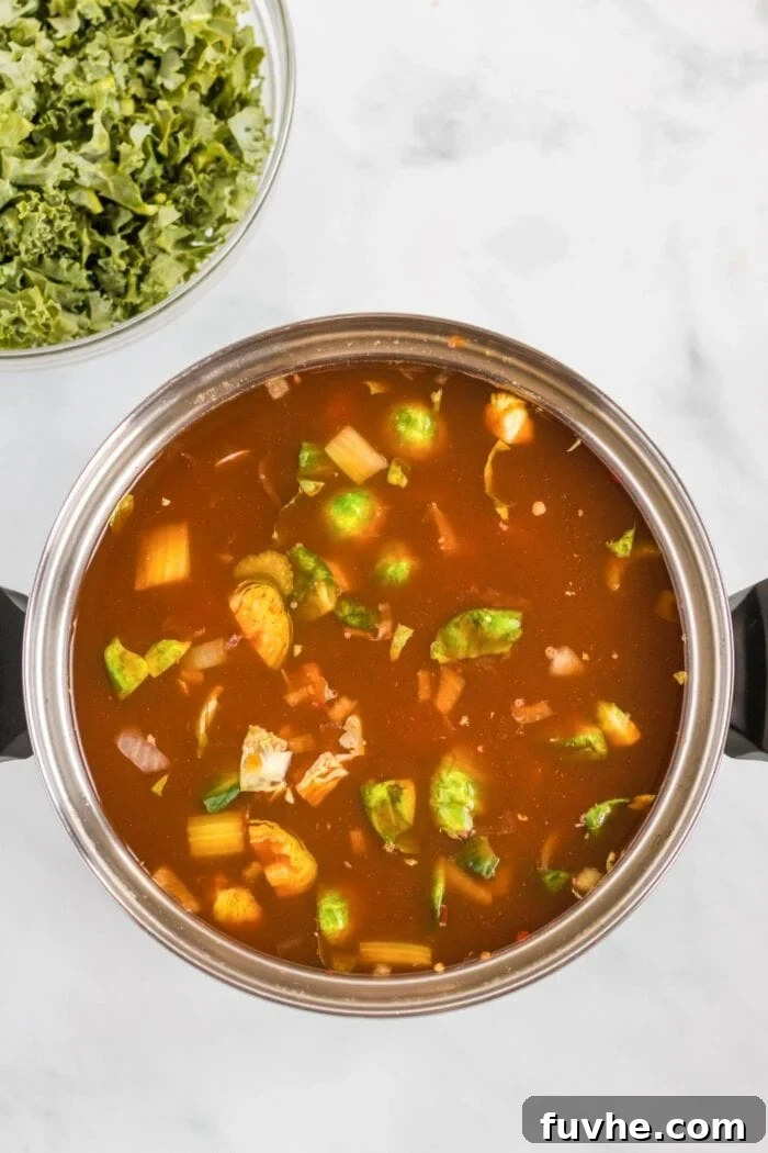 Assorted vegetables cooking in a rich, tomato-based broth within a large soup pot.