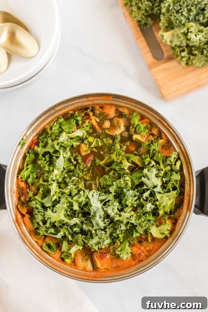 Finely chopped kale being gently stirred into a large pot of simmering lentil and tomato soup.