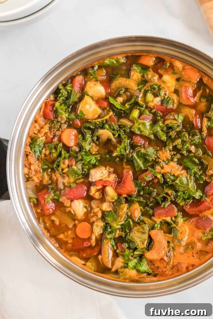 A vibrant red lentil and kale soup, enriched with tomatoes, gently simmering in a spacious soup pot on the stovetop.