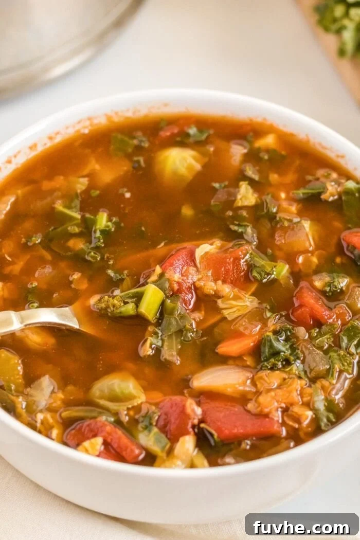 A steaming bowl of vibrant tomato and vegetable soup, with a spoon perfectly placed inside, inviting a comforting meal.