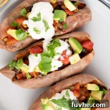 Overhead view of three sweet potatoes stuffed with black bean, corn and bell pepper and topped with sour cream, cilantro and avocado.