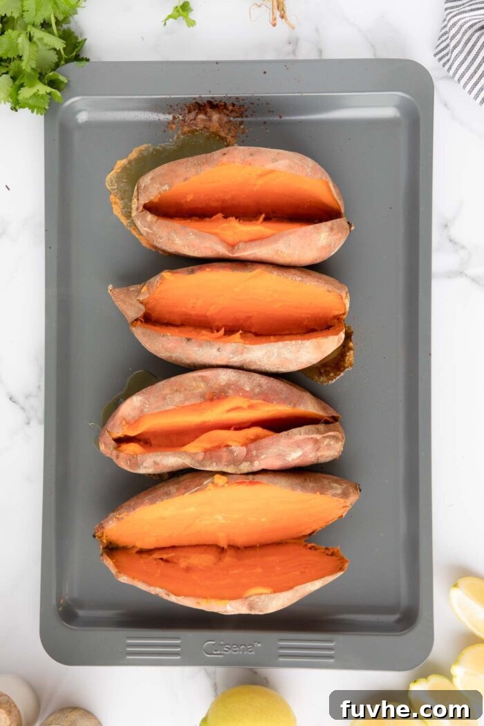4 baked sweet potatoes sliced open lengthways on a baking tray.