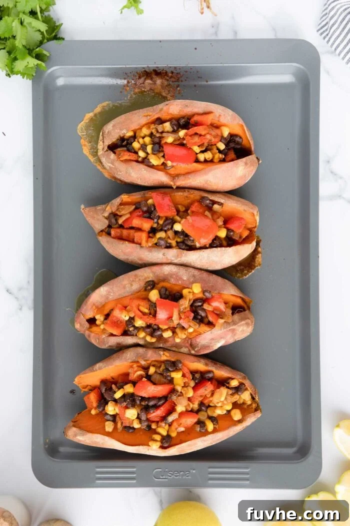 4 baked sweet potatoes stuffed with a black bean, corn and bell pepper filing on a baking tray.