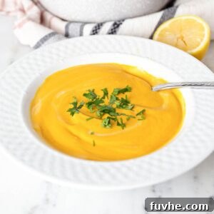 Bowl of creamy cashew carrot soup with a spoon in it.