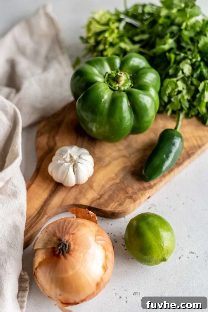 A selection of fresh, aromatic ingredients including a vibrant bell pepper, a fiery jalapeño, several cloves of garlic, a crisp onion, and a bunch of cilantro, neatly arranged on a rustic wooden cutting board, ready for preparation.